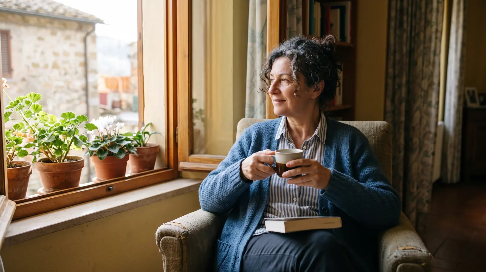Una donna sorride con una tazza di caff&egrave; vicino a una finestra soleggiata, una domenica mattina.